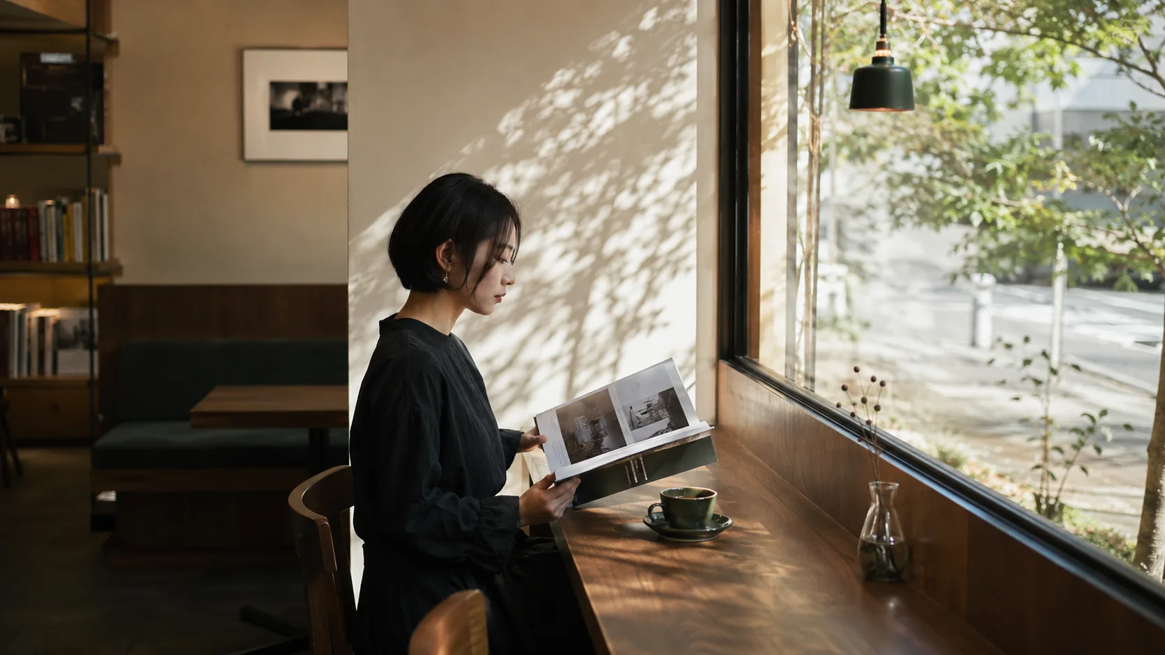 明るい窓辺の席で写真集を読む女性とコーヒーカップ